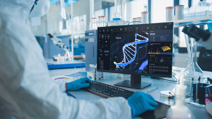 Advanced Laboratory: Medical Scientist Wearing Sterile Coverall, Face Shield and Mask Works on Computer Developing Vaccine, Drugs and Antibiotics. Screen Shows High-Tech Concept for DNA research