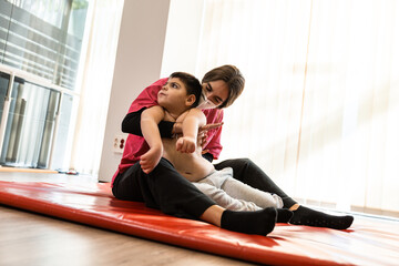 disabled child and physiotherapist on a red gymnastic mat doing exercises. pandemic mask protection