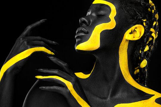 Yellow and black body paint. Woman with face art. Young girl with colorful bodypaint. An amazing afro american model with makeup.