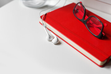 Red notebook, glasses, white earphones on white background isolated. Banner with copy space