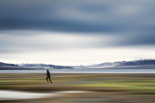 blurred view of woman walking near sea surrounded by rocky coast with snow-covered summits