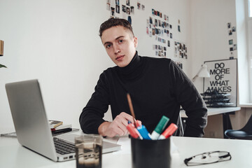 Comfortable office room and caucasian student in black sweater sitting at table there is his...