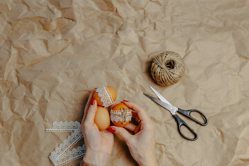 Decorating easter eggs on kraft paper with lace and rope. Three easter eggs on crumpled kraft paper background. Woman holds eggs in hands.