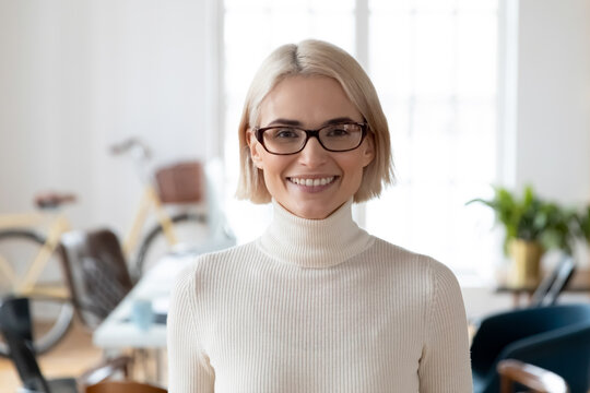 Head shot of happy professional employee posing in modern office. Profile picture of small business owner woman wearing glasses smiling at camera. Corporate portrait, female leadership concept