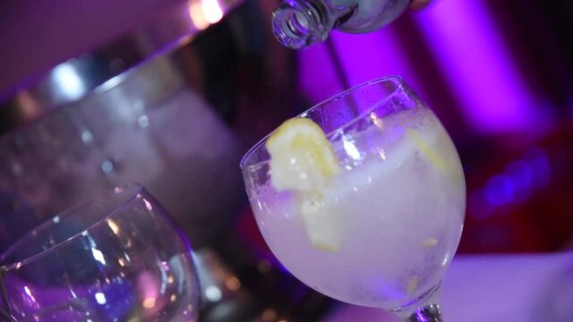 Serving drink at a party. A waiter serving a glass of gin and tonic. A crystal glass with ice cubes, lemon and gin. 