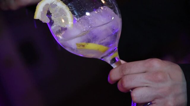 A waiter serving a glass of gin and tonic. A crystal glass with ice cubes, lemon and gin. Serving drink at a party