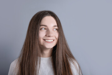 Young beautiful woman portrait with dark hair wearing white sweater looks away with a slight smile .Studio shot on gray background .Copy space.