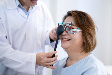 Senior Asian female patient undergoing vision check with optical trial framed, optometrist uses occluder to cover one of her eyes