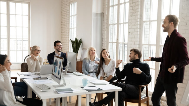 Corporate coach giving workshop to staff at meeting. Business leader discussing good sales results with his team. Presenter speaking before employees, making them laugh. Leadership, training concept