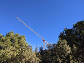 Ibiza, Spain - January 17, 2021: Bottom view, red and white crane from below appearing among the green woods with the blue sky in the background