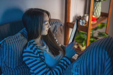 A young woman in a dark bedroom is laying in bed late at night and using her tablet to surf the Internet or read an electronic book. Concept of bedtime pastime and insomnia