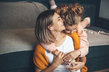 Caucasian daughter embracing her mom while she is listening music on earphones and smile