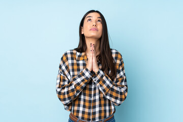 Young caucasian woman isolated on blue background keeps palm together. Person asks for something