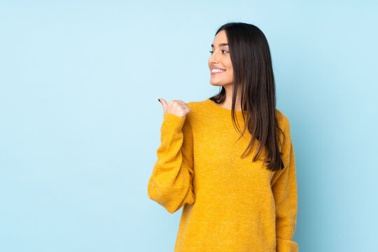 Young caucasian woman isolated on blue background pointing to the side to present a product