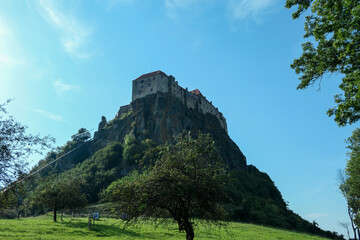 A view on Riegersburg castle in Austria. The massive fortress was build on the rock, towering above the landscape. Lush meadow underneath. Clear, blue sky above. Middle ages. Defensive structure