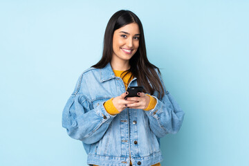 Young caucasian woman isolated on blue background sending a message with the mobile