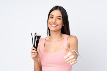 Young caucasian woman isolated on white background holding makeup brush and with thumb up