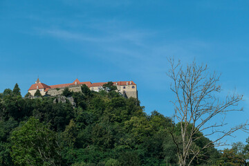 Fototapeta na wymiar Riegersburg castle in Austria towering above the area. Dense forest overgrowing the rock. Clear blue sky above the castle. The massive fortress built on the rock. Defensive structure from middle ages