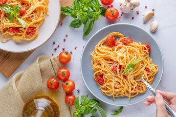 Tasty appetizing classic italian spaghetti pasta with tomato sauce, cheese parmesan and basil on plate and ingredients for cooking pasta on white marble table. Flat lay top view copy space.