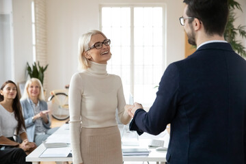 Company leader hiring female professional for job. Boss shaking hands with excited new employee at meeting. Staff applauding colleagues work achievements. CEO congratulating manager on job success.