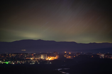 Traces of stars in the sky against the background of mountains and the city of Ivano-Frankivsk