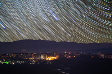 Traces of stars in the sky against the background of mountains and the city of Ivano-Frankivsk