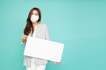 Young Asian business woman wearing face mask and showing holding blank white billboard isolated on green background