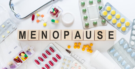 MENOPAUSE word on wooden blocks on a desk. Medical concept with pills, vitamins, stethoscope and syringe on the background.