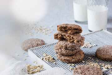Stack of homemade oatmeal cookies with oat flakes and two glasses of milk on grey background. Selective focus, horisontal orientation, copyspace