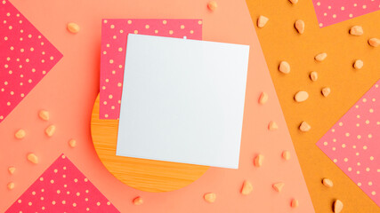 Abstract flatlay square note sheets on round wooden base,yellow beige diagonal paper background,corners of pink paper with white polka dots around perimeter,scattered pebbles.Design pattern copy space