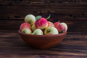 A clay bowl with apples on a wooden table.