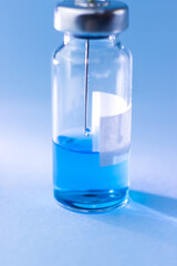 A vial with a blue vaccine with a syringe needle inside