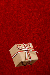 A small craft gift on red shiny background, sequins in the side. The concept for Valentine's Day. Copy space.