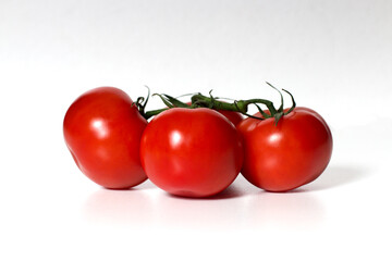 A bunch of red, ripe, round tomatoes on a green branch on a white background. Close-up. Isolated.