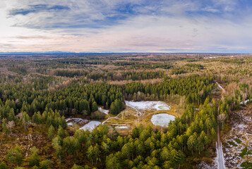 Aerial view of a small lakes inside a forest with conifer trees. Idyllic winter moment with the alp mountains in the background. Want you to have a walk here.