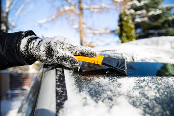 Snow clearing a car windshield in winter with a scraper.