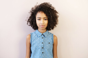 A close-up portrait of nice African preteen girl, a schoolgirl wearing polka dot shirt looks at...