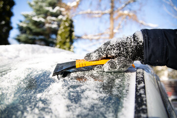 Snow clearing a car windshield in winter with a scraper.