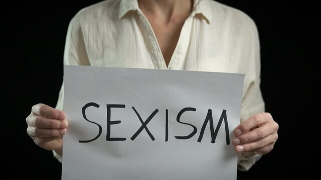 Woman against sexism. Female with a sexism poster on a black background.