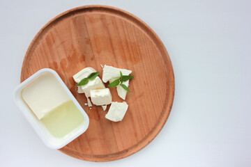 Soft feta in plastick package and sliced cheese on wooden cut board on white background. Overhead...