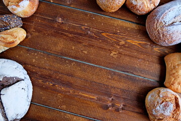 Freshly baked bread of various shapes lies on a brown wooden surface.Copy space. Top view.