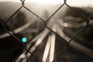 Close up of mesh fence with blurred railroad tracks in the background.