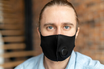 Close-up headshot of a handsome blue-eyed guy looking at the camera, wearing a protective face mask during flu season or in corona time to prevent coronavirus covid-19