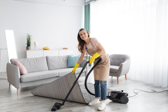 Positive female housekeeper using vacuum cleaner to tidy modern apartment. Sanitary service concept