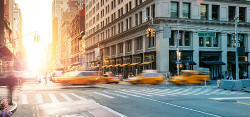 New York City - Busy intersection with yellow taxis speeding through the crowded intersection of 5th Avenue and 23rd Street with the light of sunset in the background