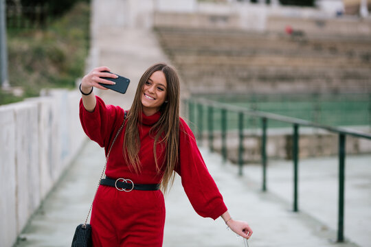 young woman with blonde hair and red dress taking a selfie in the street on a rainy day. Woman taking a selfie. Selective focus