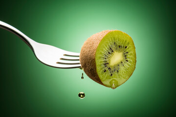 sliced kiwi fruit on fork with dripping juice on green background