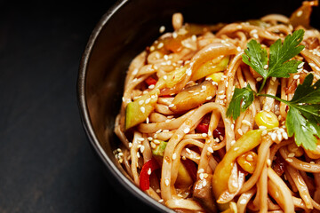 wok noodles with vegetables greens and sesame seeds in a plate on a black background