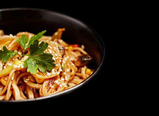 wok noodles with vegetables greens and sesame seeds in a plate on a black background