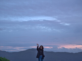 A funny girl say hi with the mountains and the sunset in the bakcground.